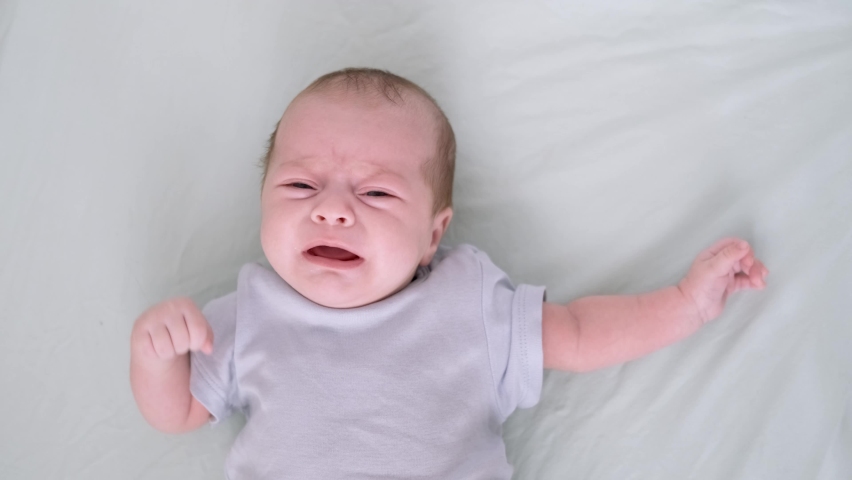 Dissatisfied, crying, upset, sad Newborn baby boy lying in nursery in crib with blue clothes on bed in bedroom at home, child crying is hungry or want to sleep Royalty-Free Stock Footage #1092647531