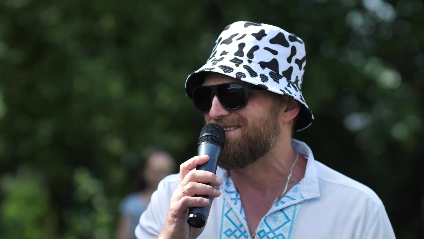Portrait of a stylish bearded man speaking through a microphone outdoors. speaker, orator, business coach speaks passionately in an open location | Shutterstock HD Video #1092647579