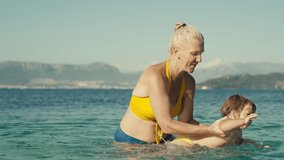 Slow motion video of grandmother and granddaughter swimming in the sea together. Woman with baby splashing water in the ocean rejoicing and smiling together.