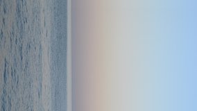 Horizon line between the surface of the sea with ripples on the water and clear blue sky with pink dawn in evening on summer. Seascape and landscape of sea ocean. Natural background. Vertical video