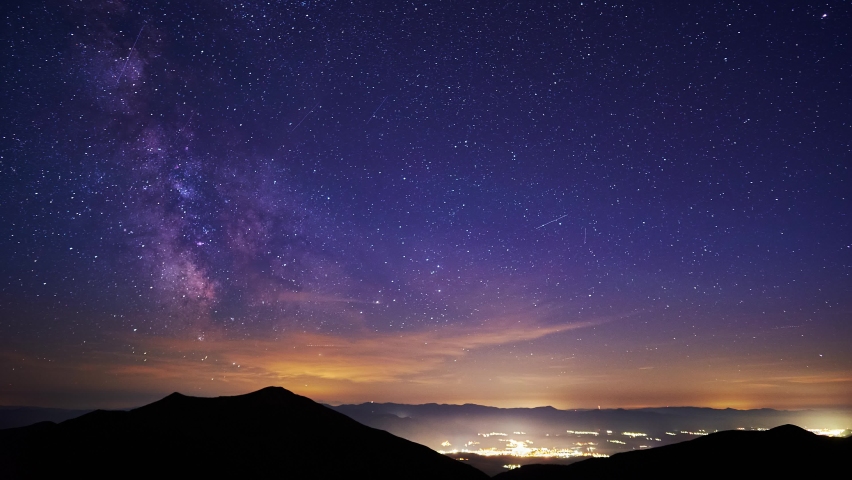 The core of the milkyway in the night sky,the silhouette of the hills and glowing city in the valley Royalty-Free Stock Footage #1092661717