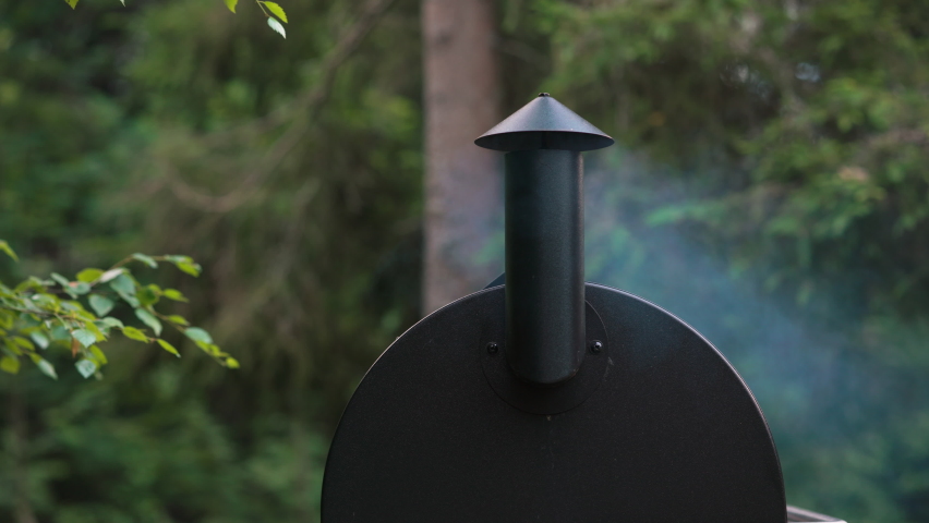 Smoke drifting out of a barbeque smoker. You cannot beat the taste of smoked foods grilled outdoors. Hearty meals in the summertime with family and friends make for wonderful memories | Shutterstock HD Video #1092668235