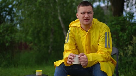 Front view portrait of handsome young Caucasian fisher sitting with coffee cup outdoors looking around. Confident concentrated man fishing outdoors in forest enjoying weekend leisure. Hobby concept