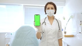 beautiful cute doctor in medical mask in medical office holds smartphone with chroma key in her hand. general practitioner. Doctor female dermatologist cosmetologist. 