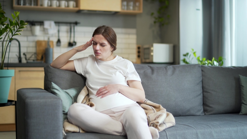 pregnant woman, feeling unwell. suffering morning sick home headache, depression during pregnancy sitting on the sofa in the living room. Indoor. unhealthy Female worries, anxiety Royalty-Free Stock Footage #1092670491