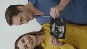 Young couple about to have new kids, isolated on white background. Young happy couple loving each other very much with baby ultrasound photo in their hands. Wedding anniversary concept.Vertical Video.