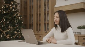 Young adult asian woman on a video call on her laptop with a christmass tree on background indoors
