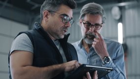 Man mechanic in glasses talking to a client in a car service and showing the results of car diagnostics and repairing on a tablet - Powered by Shutterstock - Get 15% off with code: PIKWIZARD15