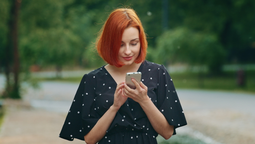 Happy female winner red-haired successful woman girl young model wins online lottery reads positive sms message in mobile phone wins sales discount in internet clothing store rejoices make yes Royalty-Free Stock Footage #1092684313