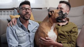 Happy gay couple sitting on floor and playing with dog at home. High quality 4k footage