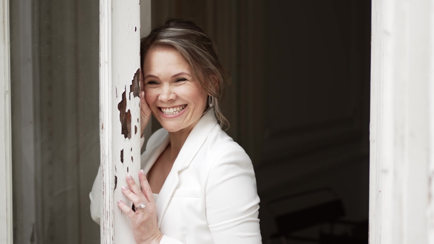 an attractive blonde woman in a white suit by the window. beautiful clothes for women. the concept of femininity and confidence.
