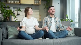 young happy couple practicing yoga during pregnancy sitting on sofa in lotus position. pregnant wife and husband spend time together, relax and meditate at home. Happiness, love and support in family - Powered by Shutterstock - Get 15% off with code: PIKWIZARD15