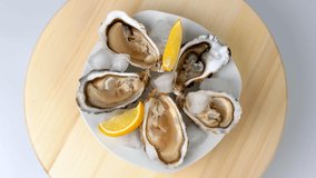 Oysters on ice with lemon closeup. Fresh Oyster on half shell on big plate in restaurant. Served table. 4K UHD video slow motion
