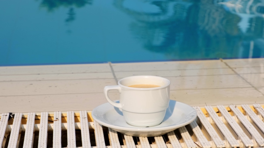 White cup of coffee or hot drink on the background of a blue swimming pool on a summer sunny day. Good morning concept and planning a new day, week, month. Vacation and travel. copy space | Shutterstock HD Video #1092717129