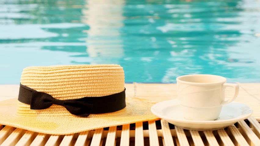 Close-up of a cup of coffee and a straw hat on the background of a blue swimming pool on a summer sunny day. Good morning concept and planning a new day, week, month. Vacation and travel. copy | Shutterstock HD Video #1092717131