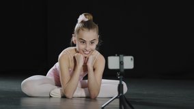 Slow motion teen girl ballerina child teenager gymnast dancer sitting on floor in dance class watching in mobile phone camera on tripod online video call conference chat with remote teacher trainer