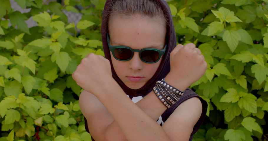 Portrait of a charismatic teenager with glasses. He crosses his arms and makes a punch with his hand. Threatening posture, demonstration of power, dominance behavior. Royalty-Free Stock Footage #1092726349