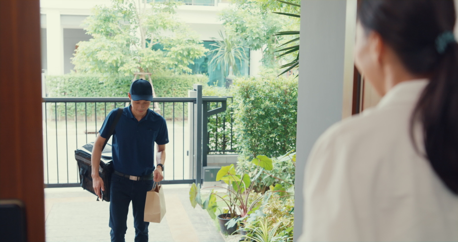 Young Asian delivery man in blue navy uniform knock door home delivery grocery online shopping to woman customer in front of the door and woman accept paper bag at house. Delivery service concept. Royalty-Free Stock Footage #1092730069