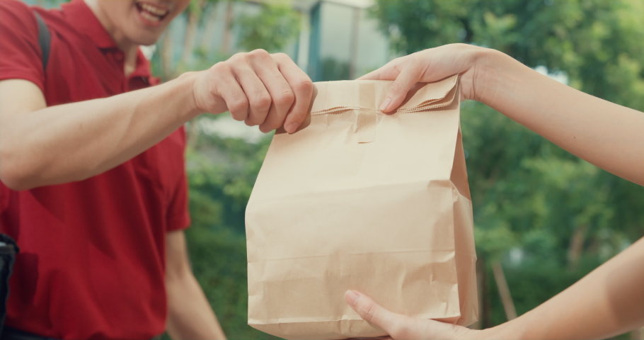 Close-up Young happy Asian delivery man with bicycle in red uniform carry case box knock door home shopping online food paper bag to woman in front of door at house. express food delivery concept. Royalty-Free Stock Footage #1092730071
