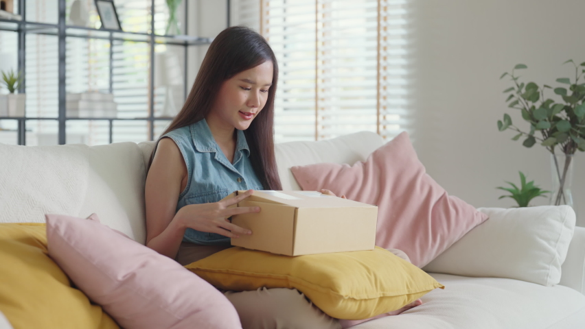 Young Gen Z influencer girl open gift postal mail box sit at home sofa couch. Asia people enjoy wow unbox carton parcel order online buy from small retail store SME shop supply chain omni channel. | Shutterstock HD Video #1092732871