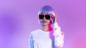 Asian woman in white sweatshirt wearing sunglasses posing moving on the purple background in 4K video.