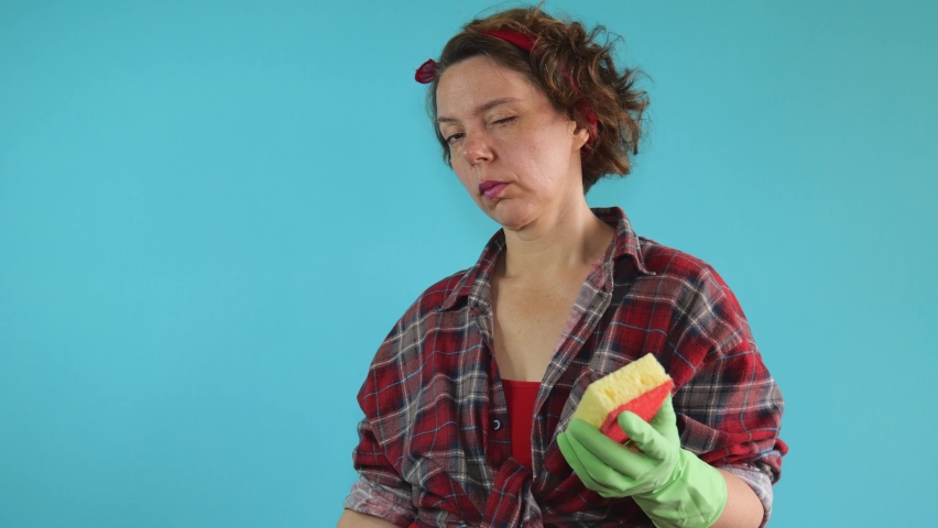 Adult cheerful pin-up cleaning woman in a plaid shirt in green gloves wipes with a washing sponge holds a yellow spray gun in her hands. Slow motion portrait. adult woman cleaning