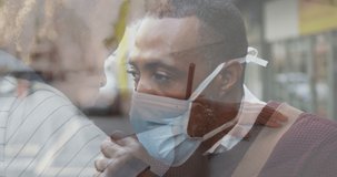 Composite video of african american man wearing face mask against boy studying at school. Covid-19 pandemic and education concept