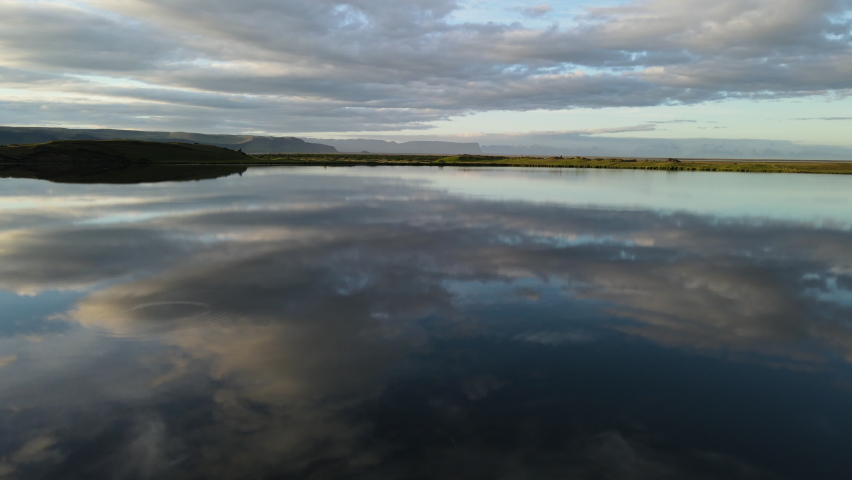 Beautiful reflexion on a lake of a cloudy sky during a sunset in Iceland. Arial shot with golden hour light over a pond, we can see mountains in bakcground. Blue sky with some clouds during a sunrise.