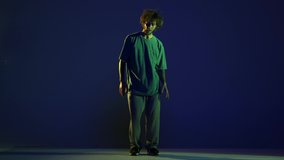 Stylish young man, hip-hop dancer wearing sport casual style outfit dancing isolated over dark blue background in neon light. Modern dance art, fashion, youth, ad, style concept. 4K, video