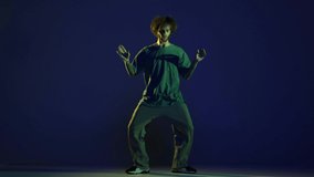 Moves. Stylish young man, hip-hop dancer wearing sport casual style outfit dancing isolated over dark blue background in neon light. Modern dance art, fashion, youth, ad, style concept. 4K, video