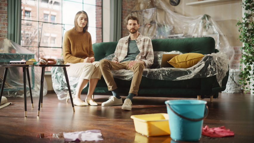 Roof is Leaking or Pipe Rupture at Home: Panicing Couple In Despair Sitting on a Sofa Watching How Water Drips into Buckets in their Living Room. Catastrophe, Distaster and Financial Ruin. Fade out Royalty-Free Stock Footage #1092746625