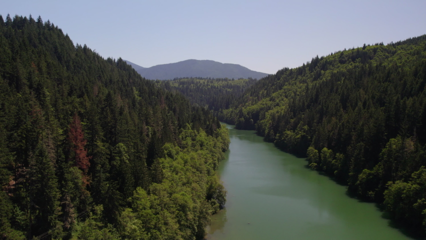 Aerial footage flying over the Nisqually River in a valley surround by a forest of evergreen trees near Le Grande Dam.