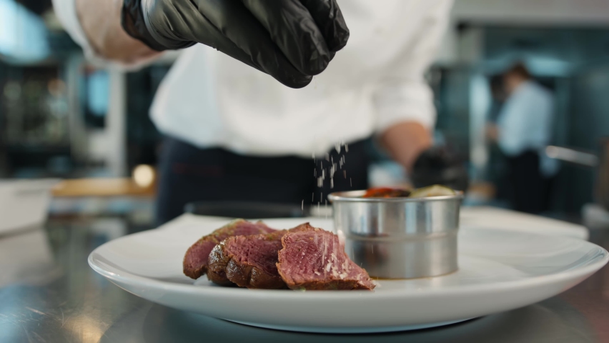 The chef sprinkles the filet mignon with coarse salt. Serving food in restaurant. Royalty-Free Stock Footage #1092752563