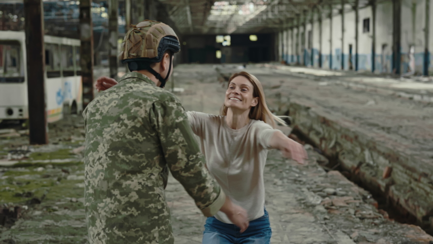 Patriotic man in soldier uniform receiving warm welcome from wife after returning from military deployment. Happy family hugging tightly while standing on destroyed factory. Royalty-Free Stock Footage #1092754707