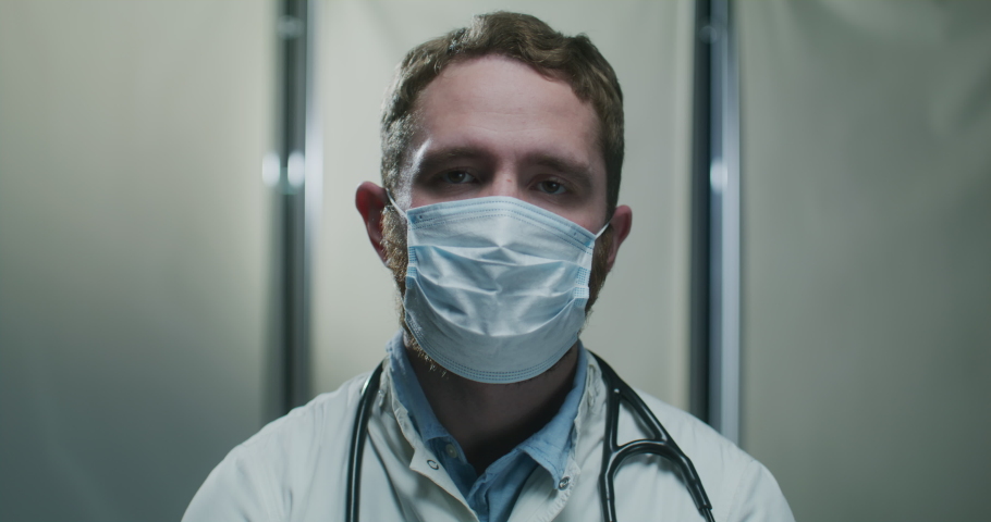 Professional Medical Worker in Face Mask Standing in Office Hospital. Portrait of a tired doctor. Portrait of Doctor Therapist Working in Clinic during Quarantine Pandemic. Royalty-Free Stock Footage #1092758401