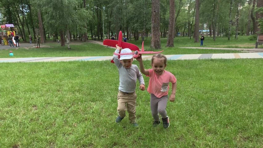 Three happy little preschool toddler children siblings kids running around have fun in summer park playing on meadow hold toy airplanes launching fly into sky. Childhood, friendship, rest, nature