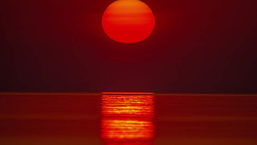 Static shot of sun rising over the Pacific ocean over the red sky with the view of sea waves below at dawn.