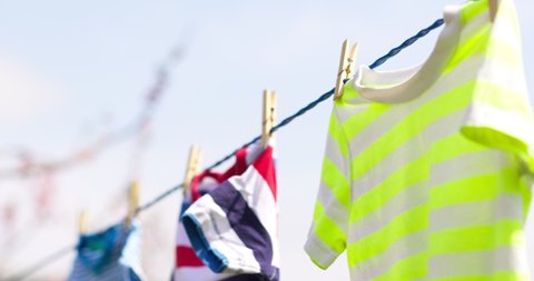 Clean clothes on rope outdoors on laundry day. Colorful t-shirts hanging on a laundry line against blue sky