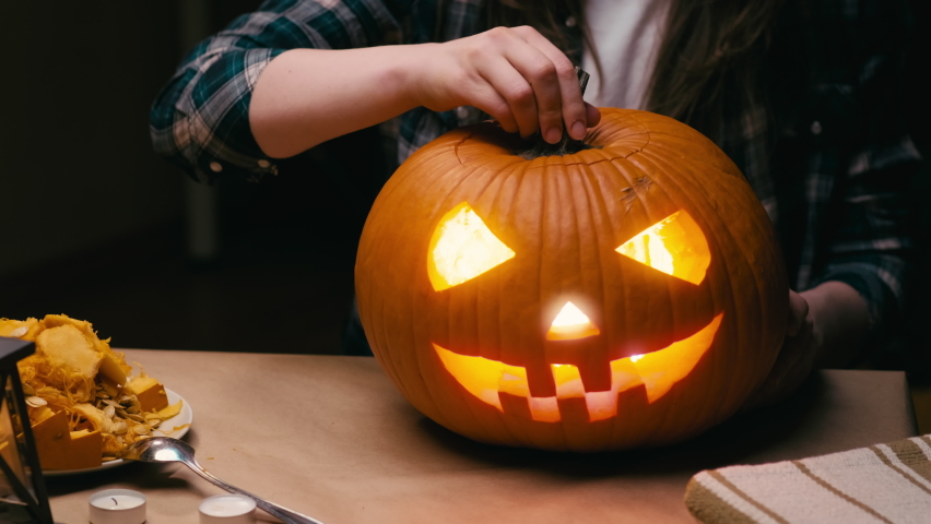 Illuminating pumpkin for Halloween. Woman sitting, lighting and showing out candle lit halloween Jack O Lantern pumpkin at home for her family. | Shutterstock HD Video #1092777137