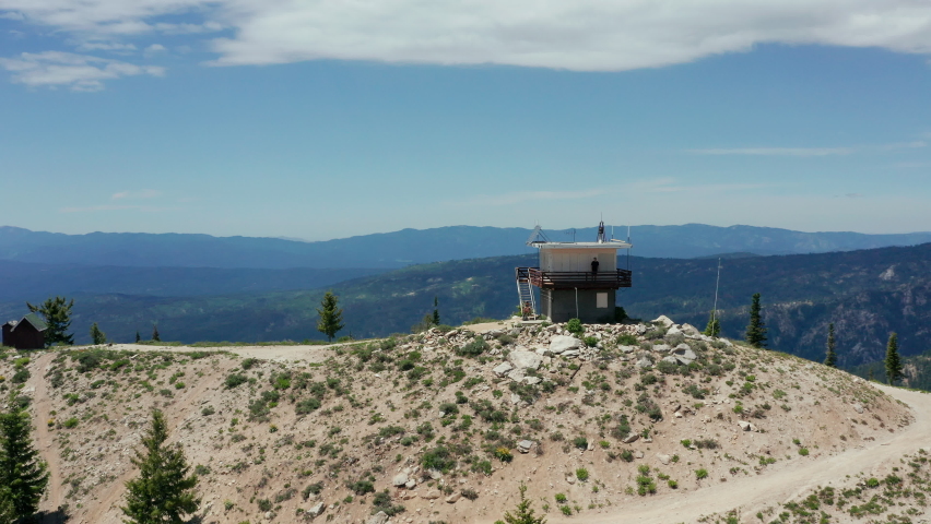Aerial circling fire lookout on top of mountain with people on lookout