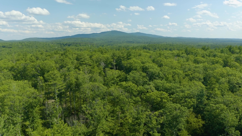 Aerial drone forward moving shot over the mountain forest beside sunset lake in New Hampshire, USA. Beautiful drone landscape.