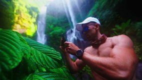 Athletic muscular people travel in tropical rainforest jungle and making video on phone beautiful waterfall on nature background 4K
