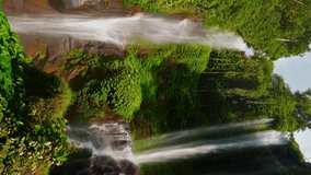 Beautiful waterfall hidden in tropical rainforest jungle on nature background 4K vertical video