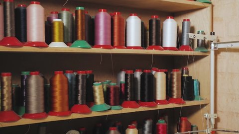 Assorted colorful spools of thread on shelves in shoemaker workshop, slow motion.