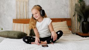 a little girl plays in a children's room with headphones and a smartphone. using a mobile phone with a headset and watching videos at home. Girl's homework using the app
