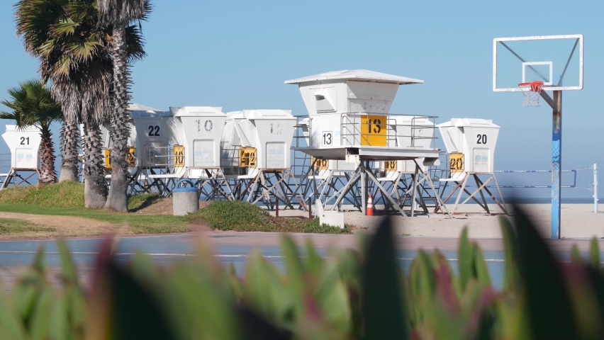Palm trees and basketball sport field or court on beach, California coast, USA. Streetball playground on shore and lifeguard stand, tower ot station. Mission beach, San Diego. Hoop, backboard and