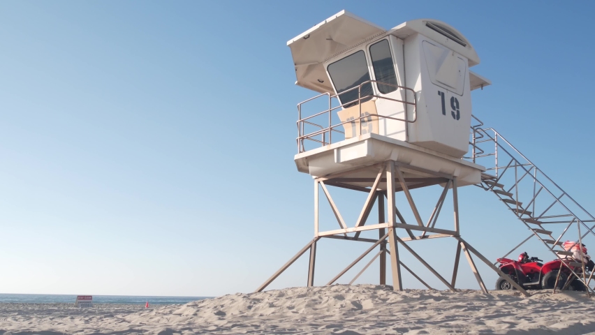 Lifeguard stand or life guard tower hut, surfing safety on California beach, USA. Summer pacific ocean aesthetic. Rescue station, coast lifesavers wachtower or house on sand. Red ATV on Mission