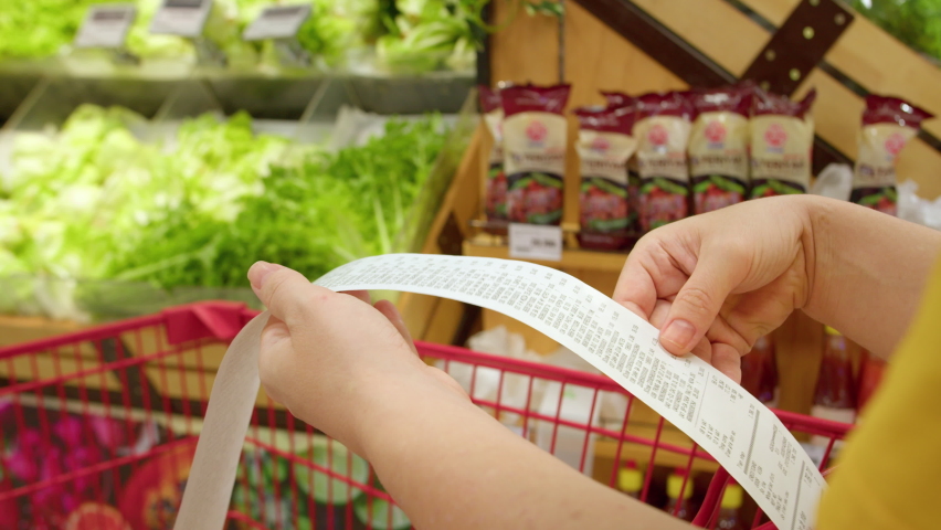 Woman checks paper check after shopping for groceries at mall by checking Dear Amount bill in a grocery cart. increase in food prices, spending money in hypermarket. Woman checking grocery store cart Royalty-Free Stock Footage #1092811945
