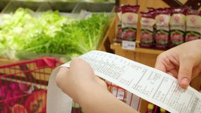 Woman checks paper check after shopping for groceries at mall by checking Dear Amount bill in a grocery cart. increase in food prices, spending money in hypermarket. Woman checking grocery store cart - Powered by Shutterstock - Get 15% off with code: PIKWIZARD15