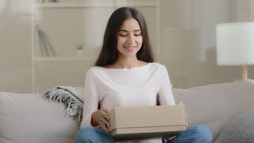 Surprised arab latin woman satisfied customer shopaholic sits on couch at home open delivery parcel postal carton box unpack present gift look at shipping goods purchases from internet clothing Royalty-Free Stock Footage #1092812489